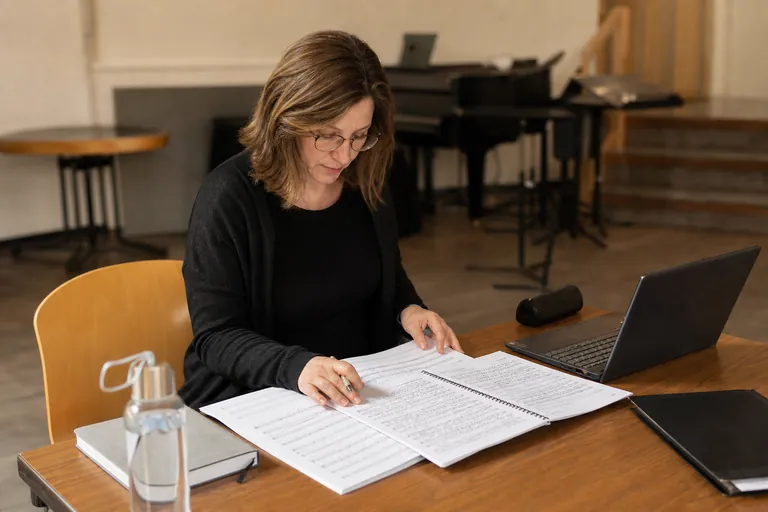 Chorleiterin vergleicht Programmheft und Partituren für eine Musikfolgenmeldung.